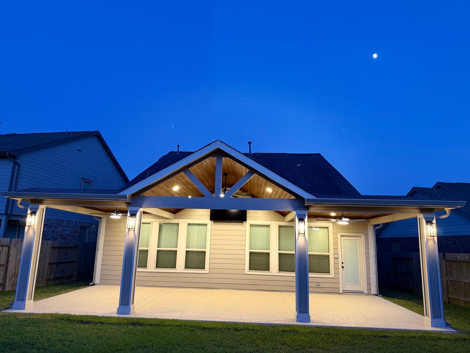 Same backyard after Lira Construction LLC installed a custom gable patio cover, lit up at dusk