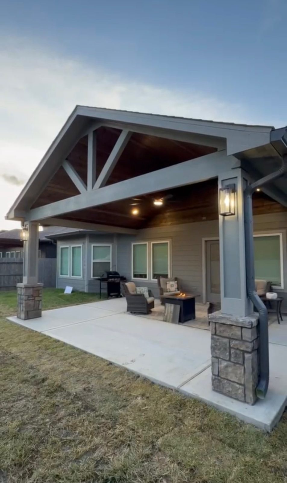 Patio cover with stone-clad columns and outdoor fire pit at dusk